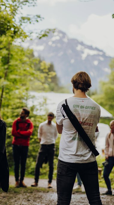 Gruppen von Menschen im Wald, die an einer geführten Tour teilnehmen, mit Berg und Bäume im Hintergrund. | © Kleinwalsertal Tourismus eGen • Fotograf: Philip Herzhoff