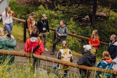 Gruppe von Menschen beim Outdoor-Workshop in einem grünen Park mit Bäumen und Wegen.
